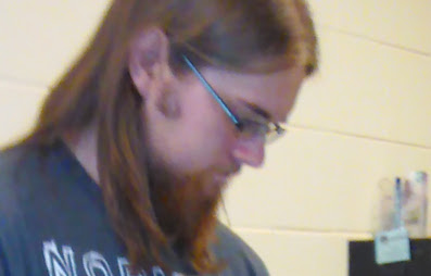 A photo of Nick. He has shoulder-length brown hair, thin glasses, and a thick goatee.